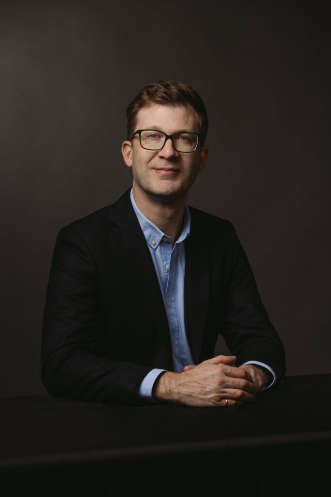 A portrait of Jeremy Boland, seated, hands clasped.